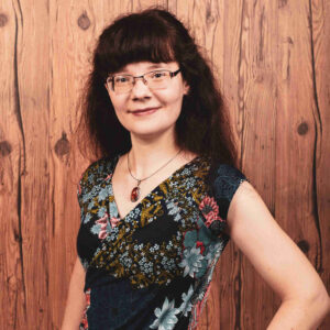 Foto der Autorin Alicia Hartung in einem floralen Kleid vor braunem Holz; dem Hintergrund ihres Blogs "Aus der Schublade"